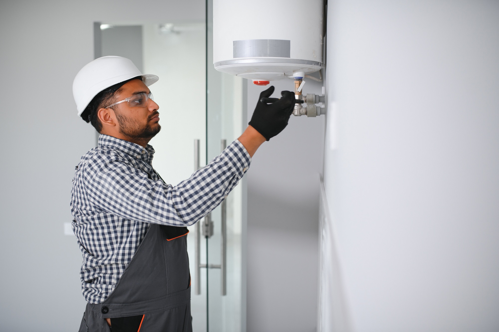 Indian plumber using screwdriver while fixing boiler or water heater, working on heating system