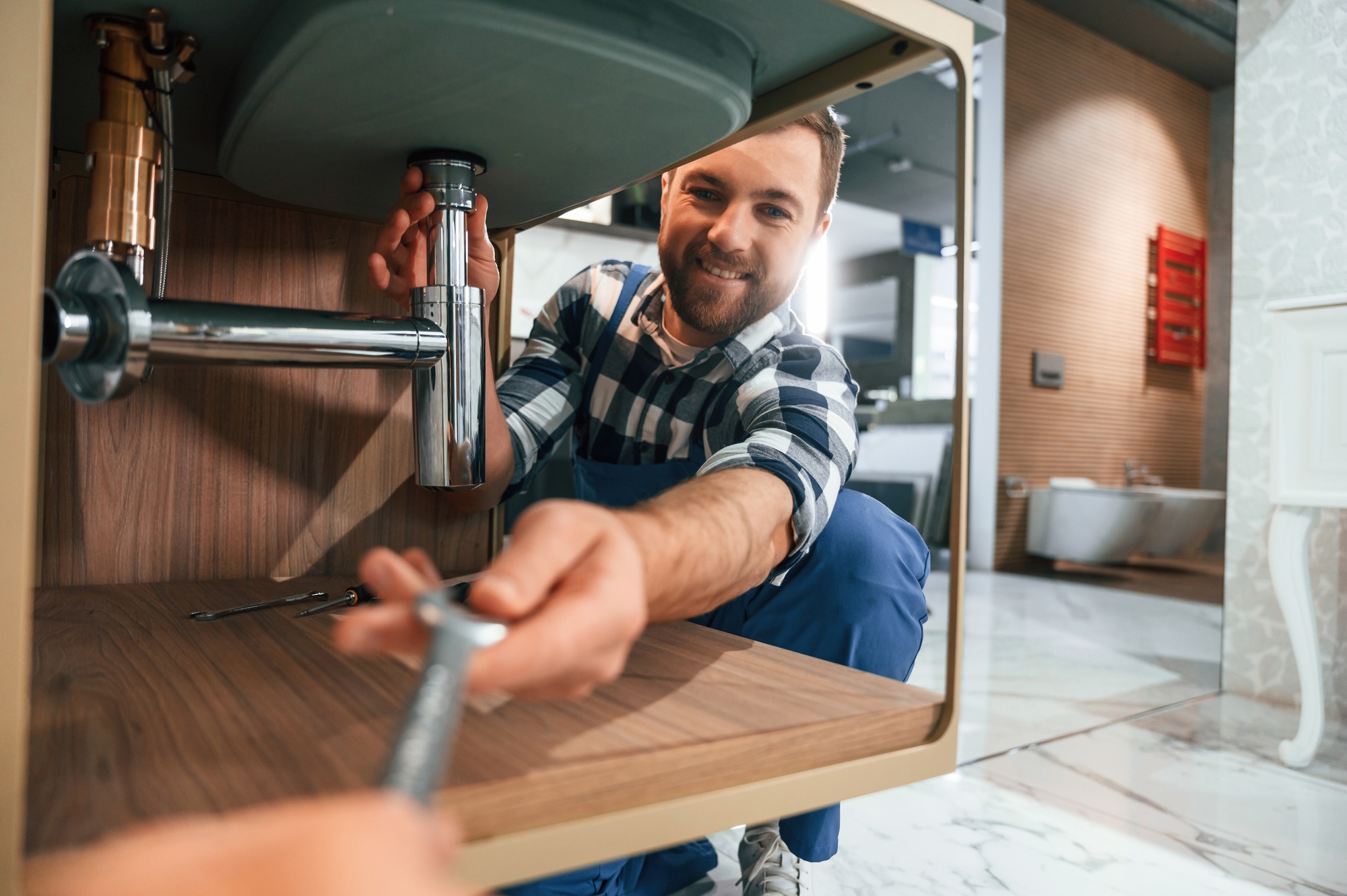Taking a wrench. Plumber in blue uniform is at work in the bathroom